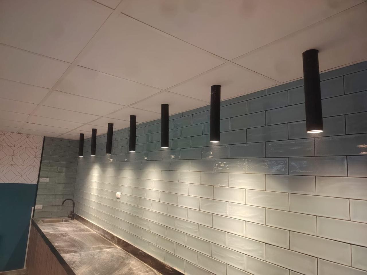 Pasillo comercial con cielo americano instalado y luminarias colgantes sobre revestimiento de muro gris