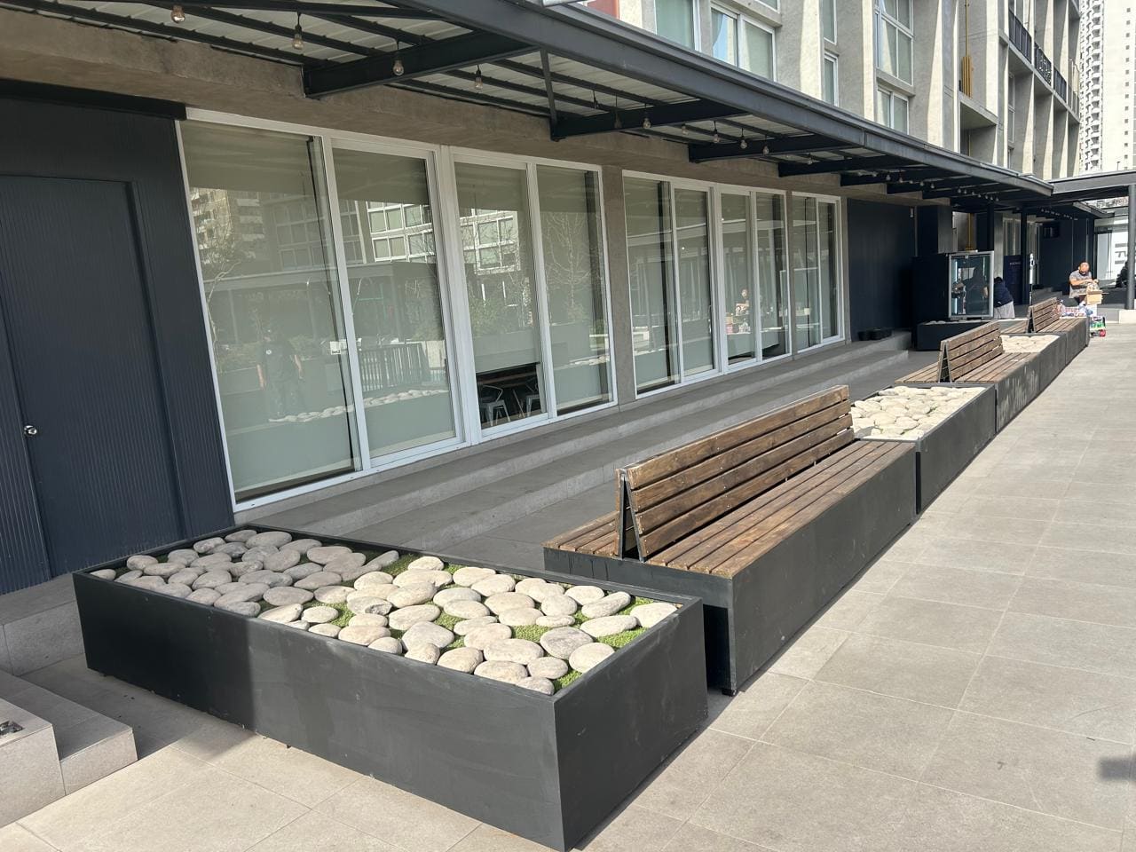 Jardineras rellenas con piedra blanca y escaños de madera a lo largo de una fachada comercial