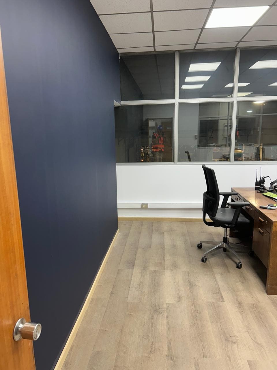Oficina con piso flotante instalado y muro pintado en azul profundo, con puesto de trabajo al fondo